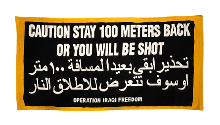 A black banner in both English and Arabic that reads: ‘caution stay 100 meters back or you will be shot’