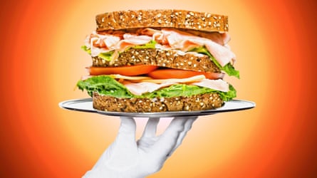 A gloved hand holds up a sandwich on a platter.