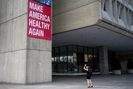 A woman takes a photograph of a banner that says ‘Make America Healthy Again’