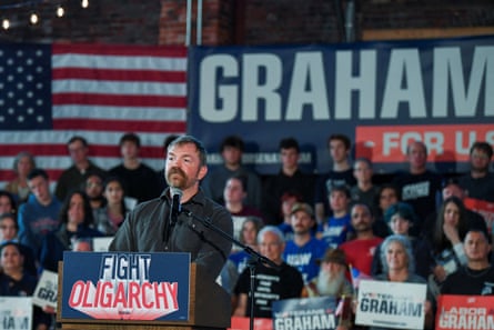man stands at podium marked 'fight oligarchy' at rally