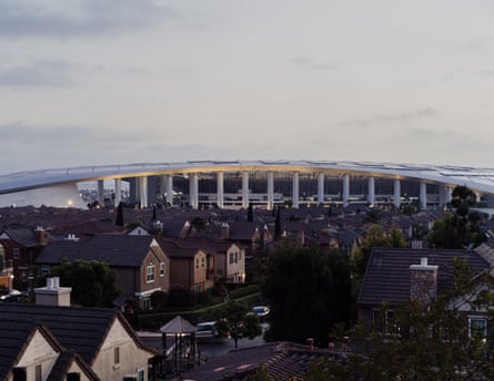 homes in a gated community are seen in the foreground with a large stadium directly behind it in the background